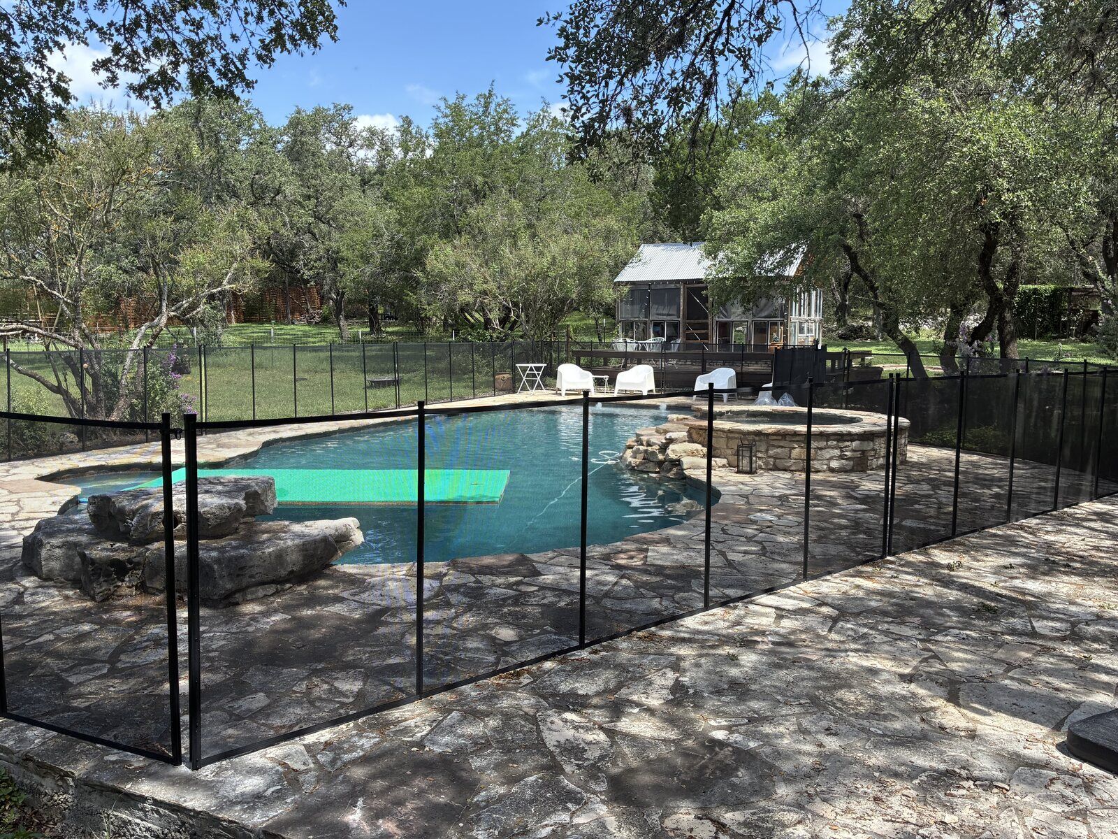 Removable mesh pool fence enclosing a ranch pool, spa, and stone waterfall on a flagstone deck in Wimberley TX, All-Safe certified