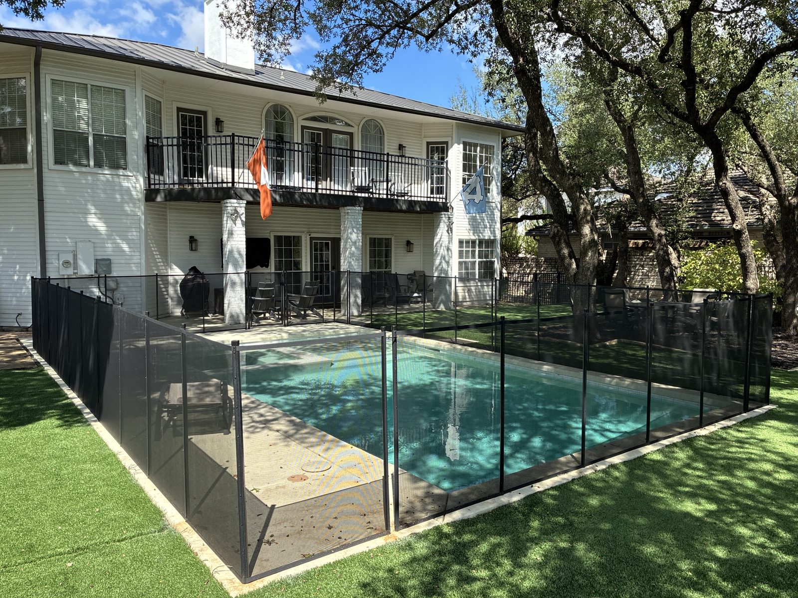 Removable mesh pool fence enclosing a rectangular pool and spa under live oaks in Lakeway TX, All-Safe certified